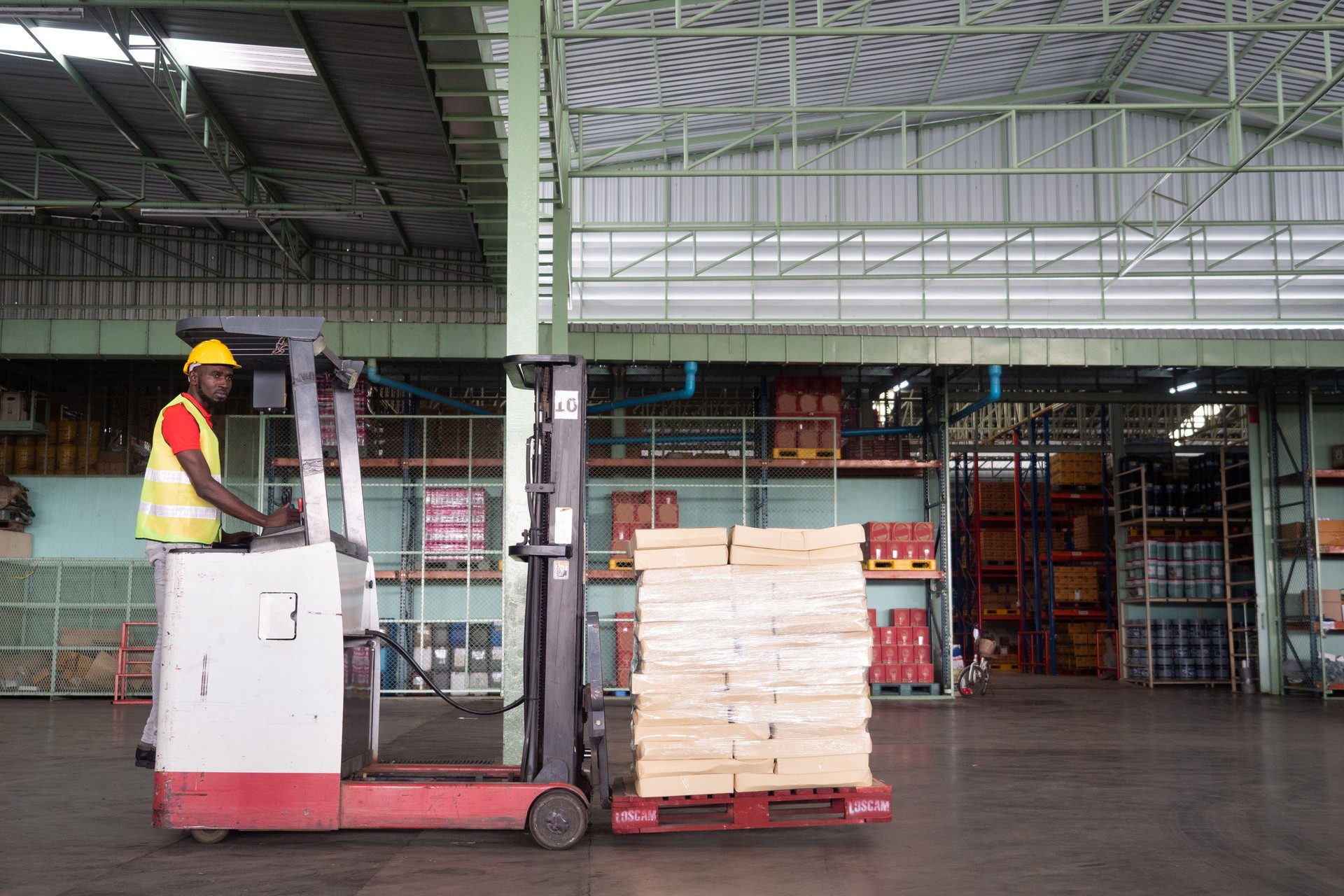 African man worker with forklift in storage warehouse.
